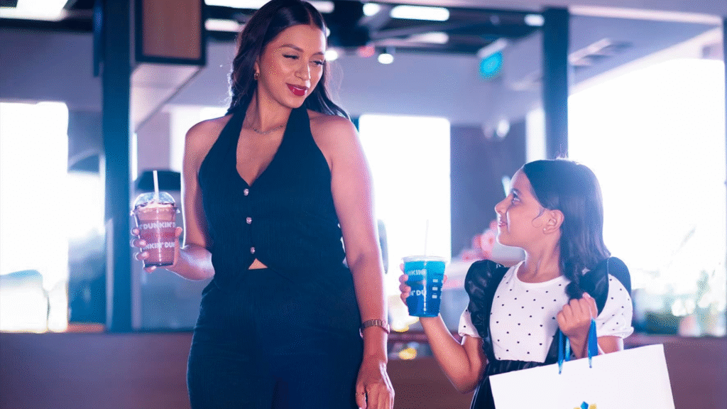 Madre e hija disfrutando de una bebida y compras con bolsas de Mall Premier frente a Dunkin'.