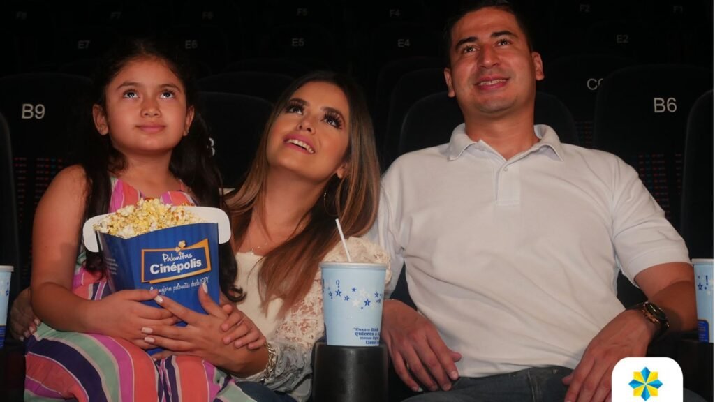 Familia sonriendo mientras disfruta de una película en las cómodas butacas de las salas de cine de Mall Premier Juticalpa, comiendo palomitas.