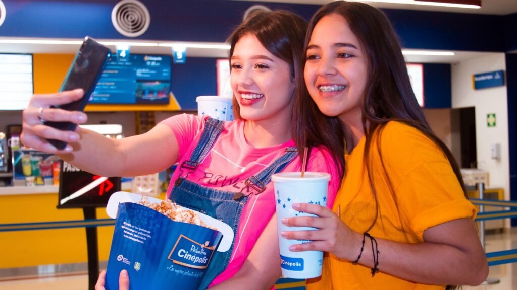 Dos amigas sonrientes tomándose una selfie con sus palomitas y bebidas en el lobby del cine de Mall Premier Juticalpa antes de ver una película.