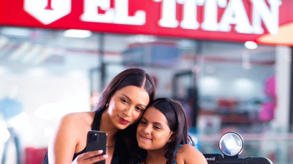 Niña sonriendo mientras conduce un coche de juguete blanco dentro de Almacenes El Titán en Mall Premier Catacamas, con su madre detrás.