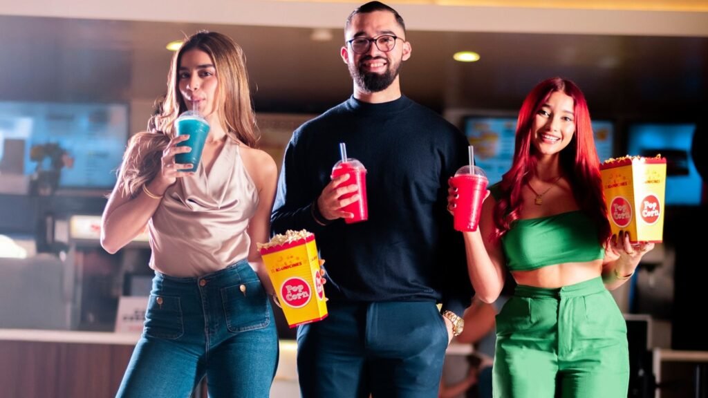 Tres amigos sonriendo con palomitas y refrescos en el lobby del cine en Mall Premier Comayagua, listos para una tarde de películas.