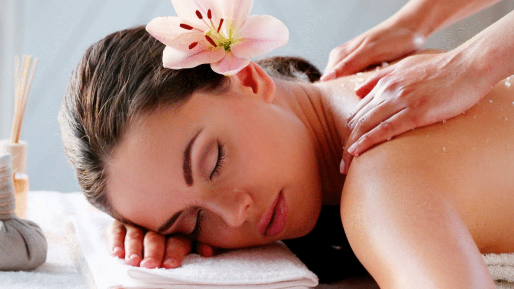 Mujer recibiendo un masaje de espalda con exfoliante y una flor de lirio sobre su hombro en Thalassa Spa.