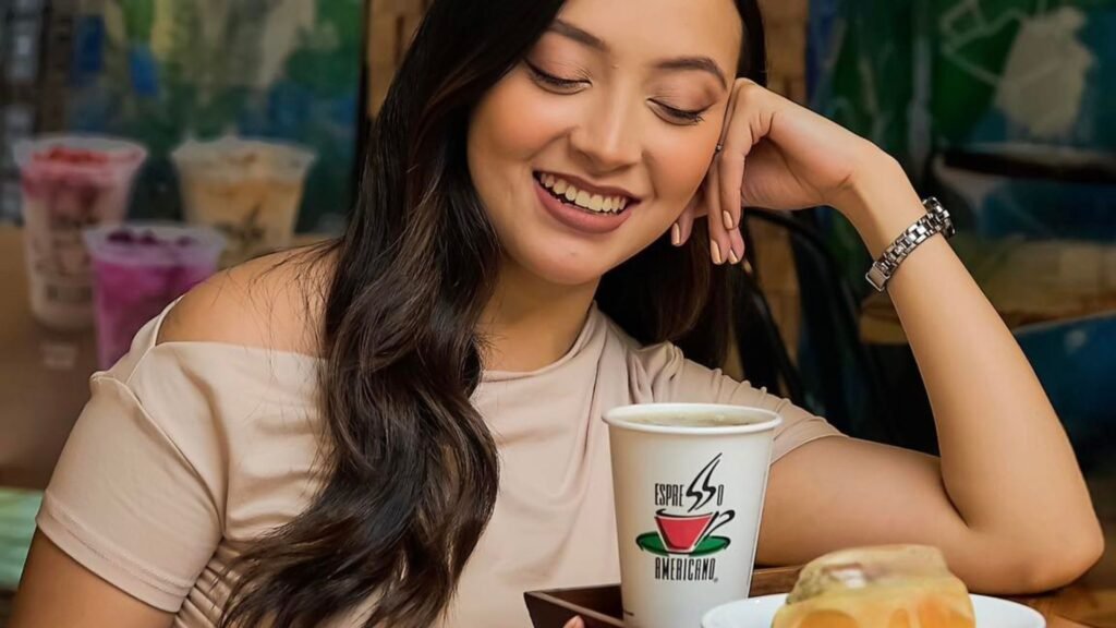 Mujer disfrutando de un momento de relajación con un capuchino y un cinnamon roll de Espresso Americano en el ambiente moderno de Mall Premier Comayagua.