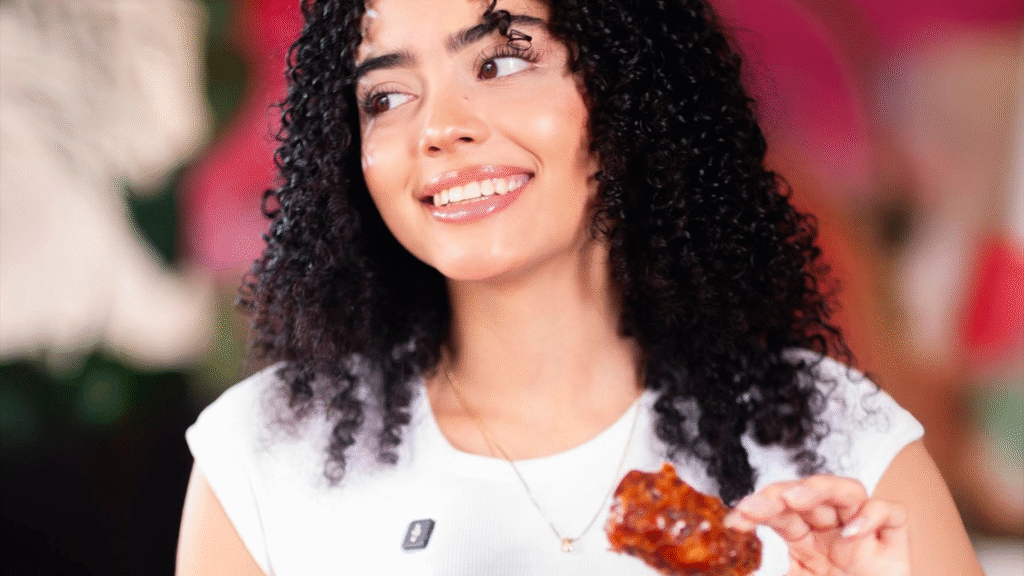 Mujer joven sonriendo mientras sostiene un ala de pollo en salsa BBQ en el restaurante Indigo Café.