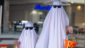 Mamá e hijo disfrazados de fantasmas con lentes de sol sosteniendo baldes de calabaza para dulces en el evento FantasMall de Mall Premier.