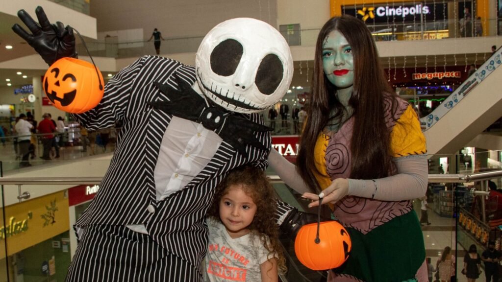 Personas disfrazadas de Jack Skellington y Sally posando para una foto con una niña durante el evento de Halloween FantasMall de Mall Premier.