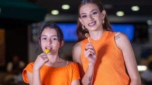 Madre e hija vestidas de naranja disfrutan de unas paletas durante la celebración de Halloween en evento Spooktacular de Plaza Premier