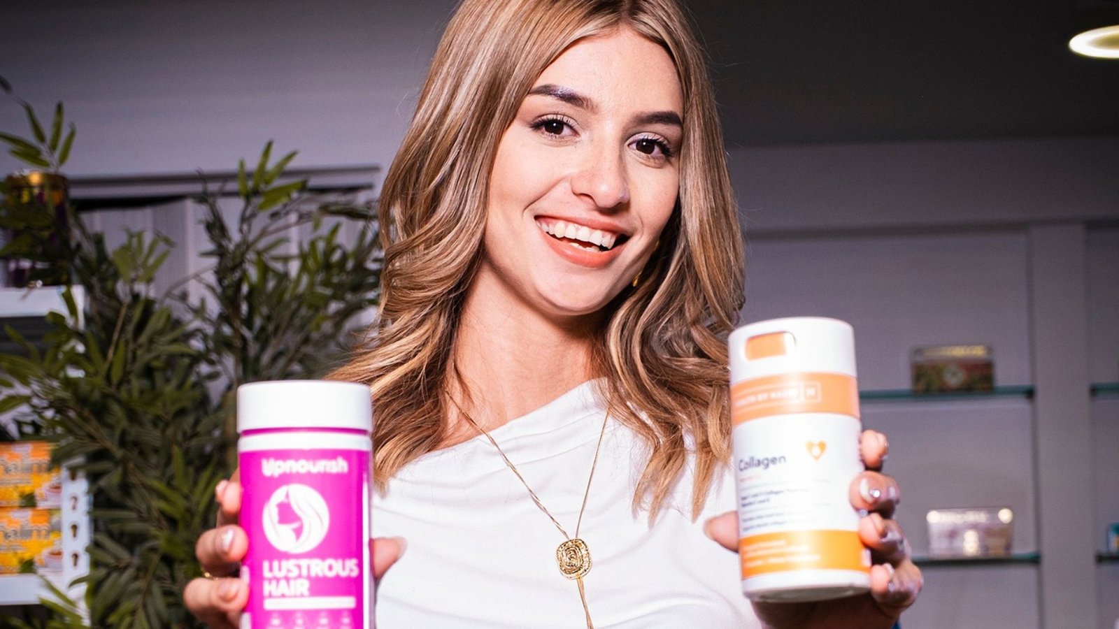 Mujer sonriendo y sosteniendo dos envases de suplementos dietéticos, uno de Lustrous Hair y uno de Collagen.