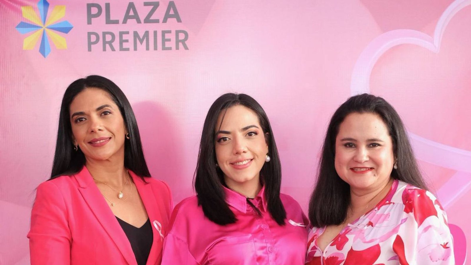 Tres mujeres posan frente al backdrop rosa de Plaza Premier Humuya durante la actividad “The Women Boss”, en conmemoración del Día de la Mujer Hondureña, representando liderazgo, unión y empoderamiento femenino.
