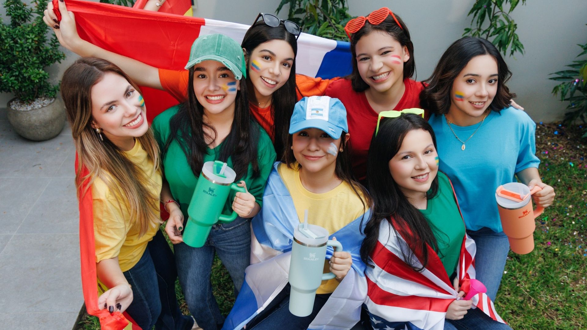 Grupo de jóvenes aficionadas con rostros pintados sosteniendo termos Stanley de colores, un accesorio ideal de Lady Lee en Mall Premier.