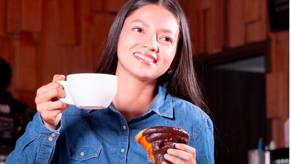 Estudiante universitaria disfrutando un café y un postre de chocolate en un food court de plaza comercial