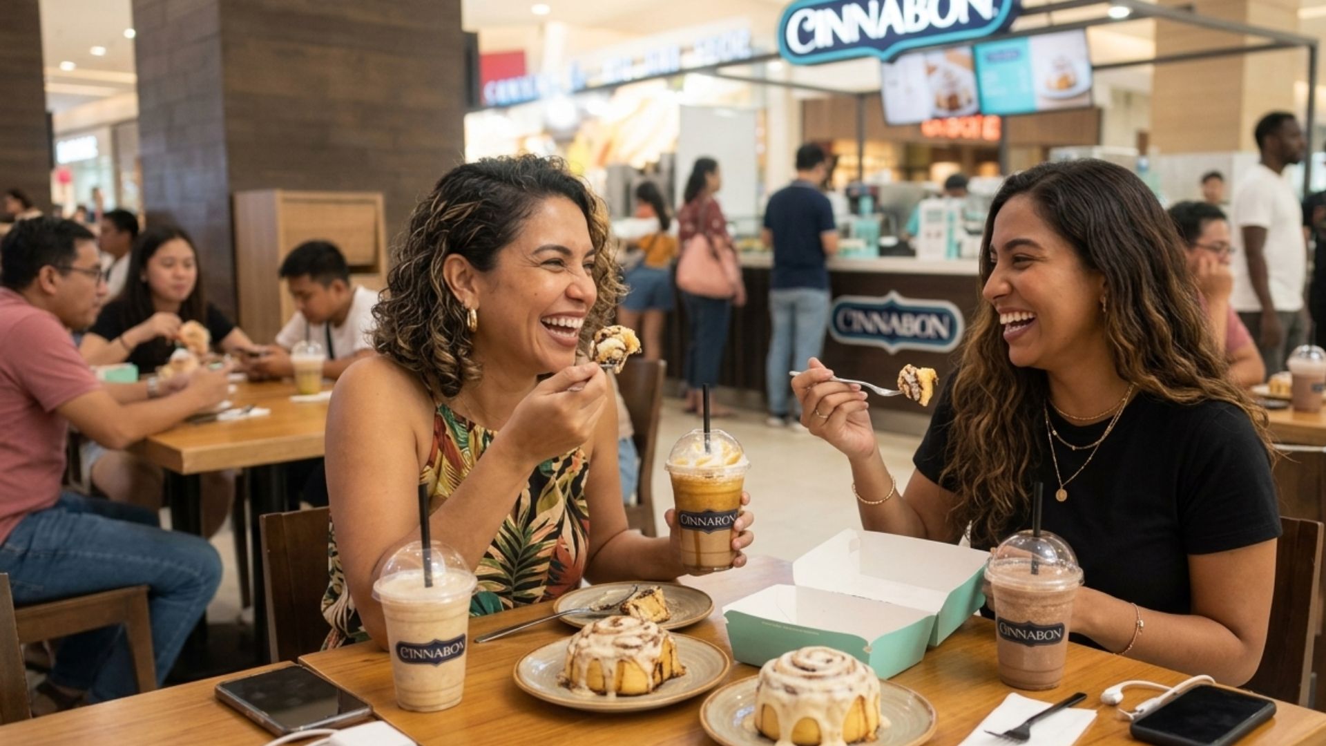 Amigas disfrutando rollos de canela y bebidas heladas, destacados entre los postres en Honduras en Cinnabon de Mall Premier.  